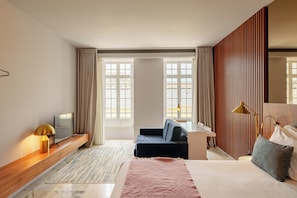 Une chambre d’hôtel moderne équipée d’un lit, d’un bureau, d’un canapé, d’une télévision et de grandes fenêtres.
