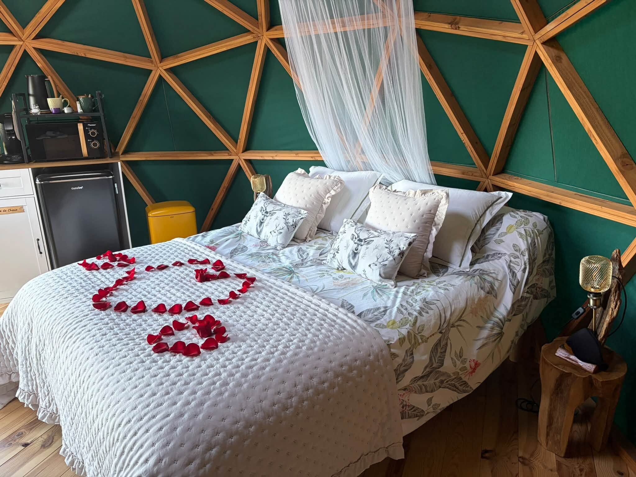 Een bed met een bloemenlaken, een rozenblaadjes-hart en een hemelbed.