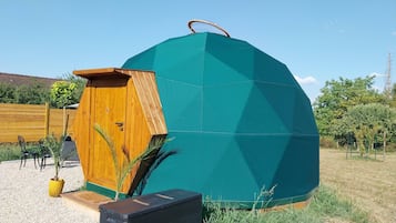 Een groene geodetische koepel met een houten deur en een klein terras.