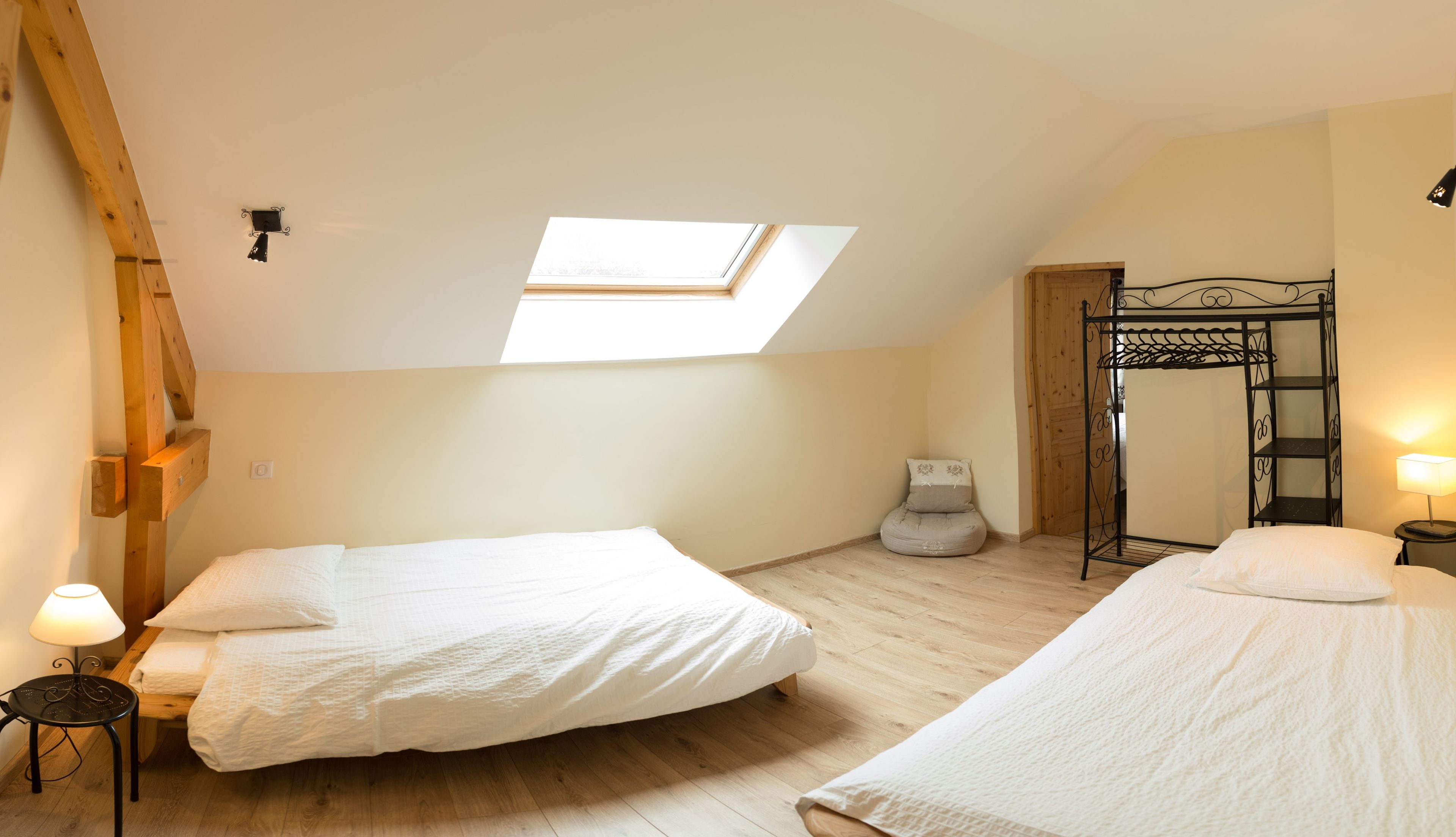 Een slaapkamer met twee bedden, een dakraam, een houten ladder en een klein nachtkastje met een lamp.