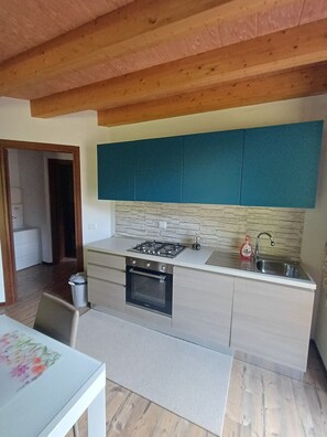 Eine kompakte Küche mit Gasherd, Backofen und Spüle, Holzbalkendecke und Türkis-Schränken.