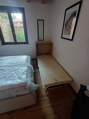 Ein Zimmer mit einem Bett, einem kleinen Nachttisch, einem Fenster und einem gerahmten Bild an der Wand.