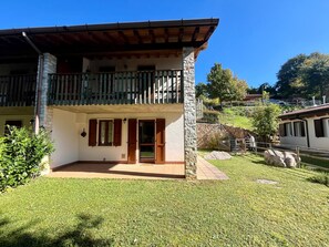 Ein zweistöckiges Gebäude mit Balkon, Steinpfeilern und einem gepflegten Rasen.