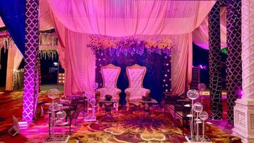 A stage with two ornate chairs, draped curtains, and floral arrangements.