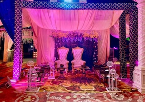 A stage with two ornate chairs, draped curtains, and floral arrangements.