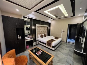 A modern hotel room with a bed, a seating area, a TV, and a minibar.