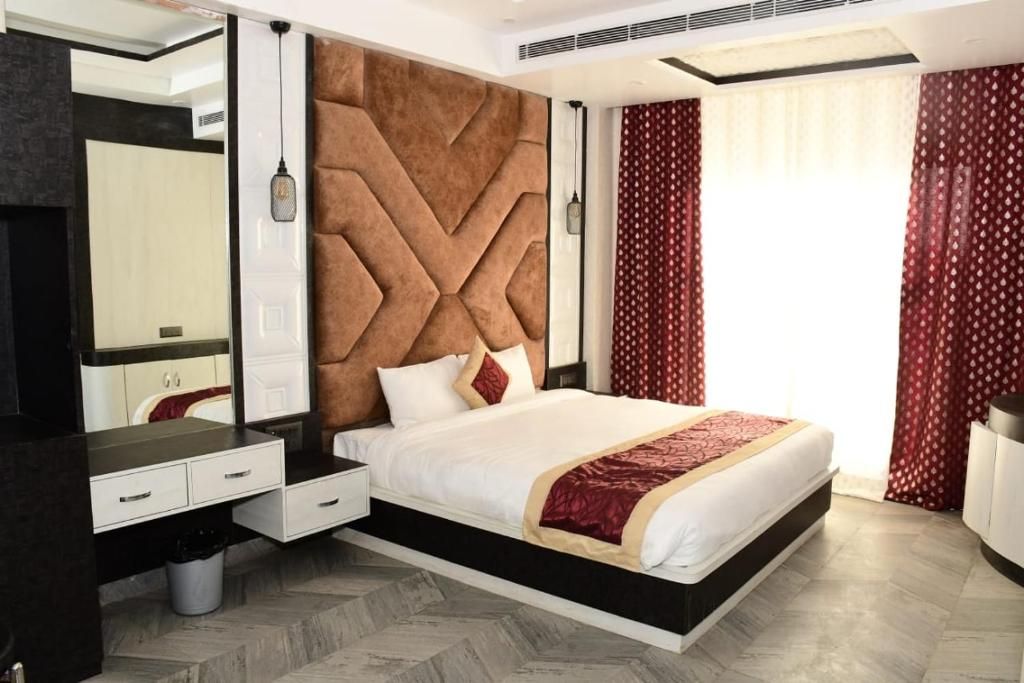 A modern bedroom with a large bed, a built-in wardrobe, a mirror, and a window with curtains.