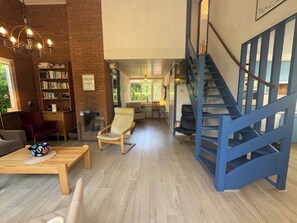 A spacious living area with a wooden coffee table, a rocking chair, and a bookshelf. A blue staircase is visible in the background. - Holiday home with a large garden, near Lake Grevelingen (Brouwershaven)