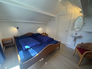 Een slaapkamer met een bed, nachtkastjes, een spiegel en een rieten stoel.
