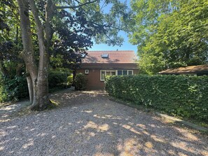 A house with a gravel driveway, surrounded by trees and a hedge. - Holiday home with a large garden, near Lake Grevelingen (Brouwershaven)