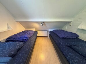 A small, compact room with two single beds, a wooden floor, a white radiator, and a slanted ceiling. - Holiday home with a large garden, near Lake Grevelingen (Brouwershaven)