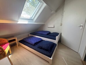 A dormitory room with a sloped ceiling, two beds with blue bedding, a wooden chair, and a small table. - Holiday home with a large garden, near Lake Grevelingen (Brouwershaven)