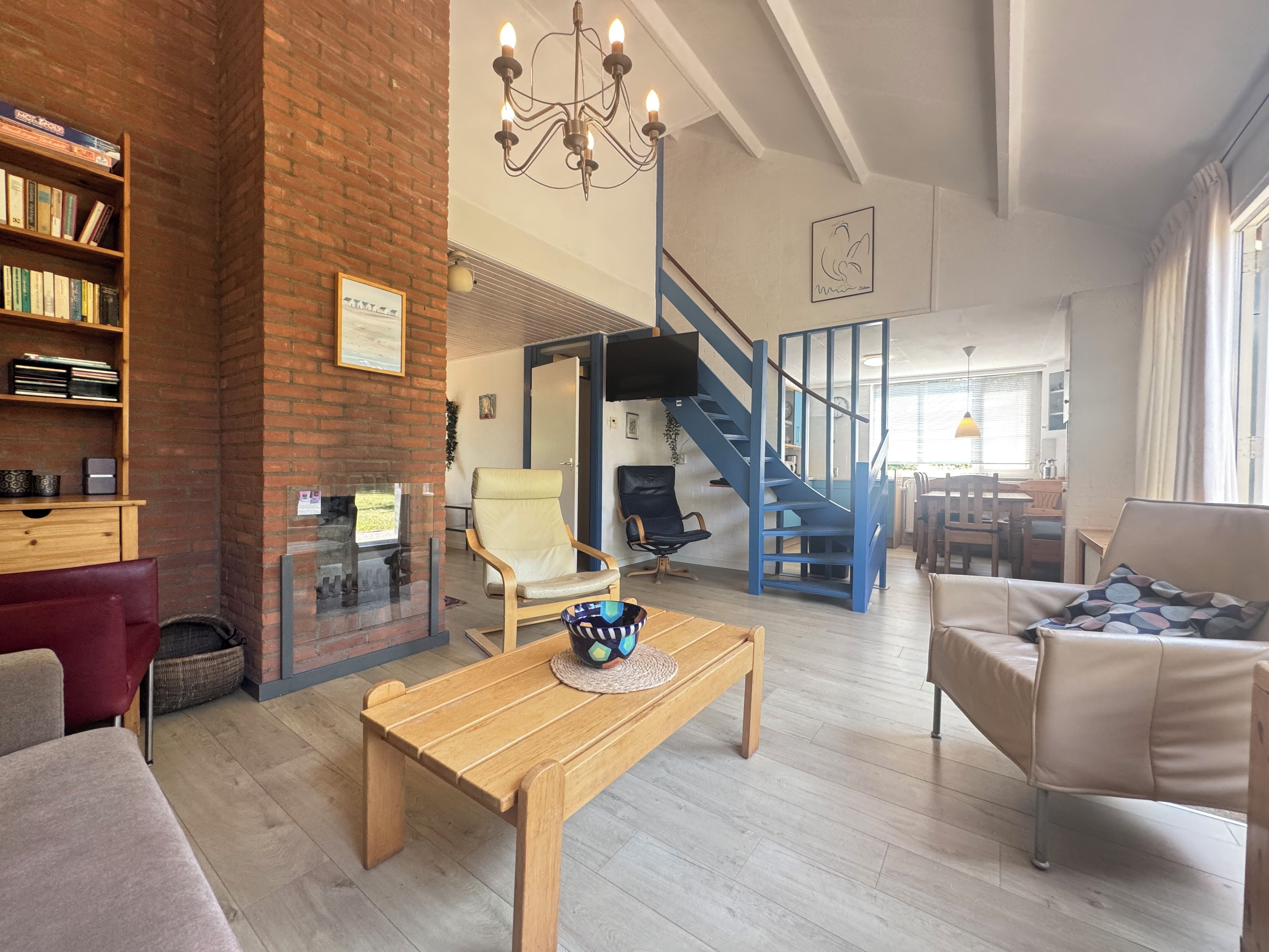 Een ruime woonkamer met een houten salontafel, een leren bank, een boekenkast en een trap naar een ander niveau.