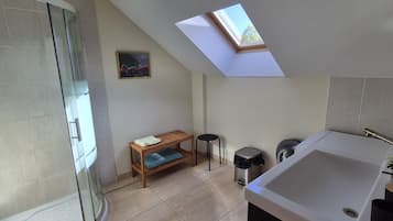 A modern bathroom with a skylight, a glass shower enclosure, a wooden bench, a small stool, and a large bathtub.