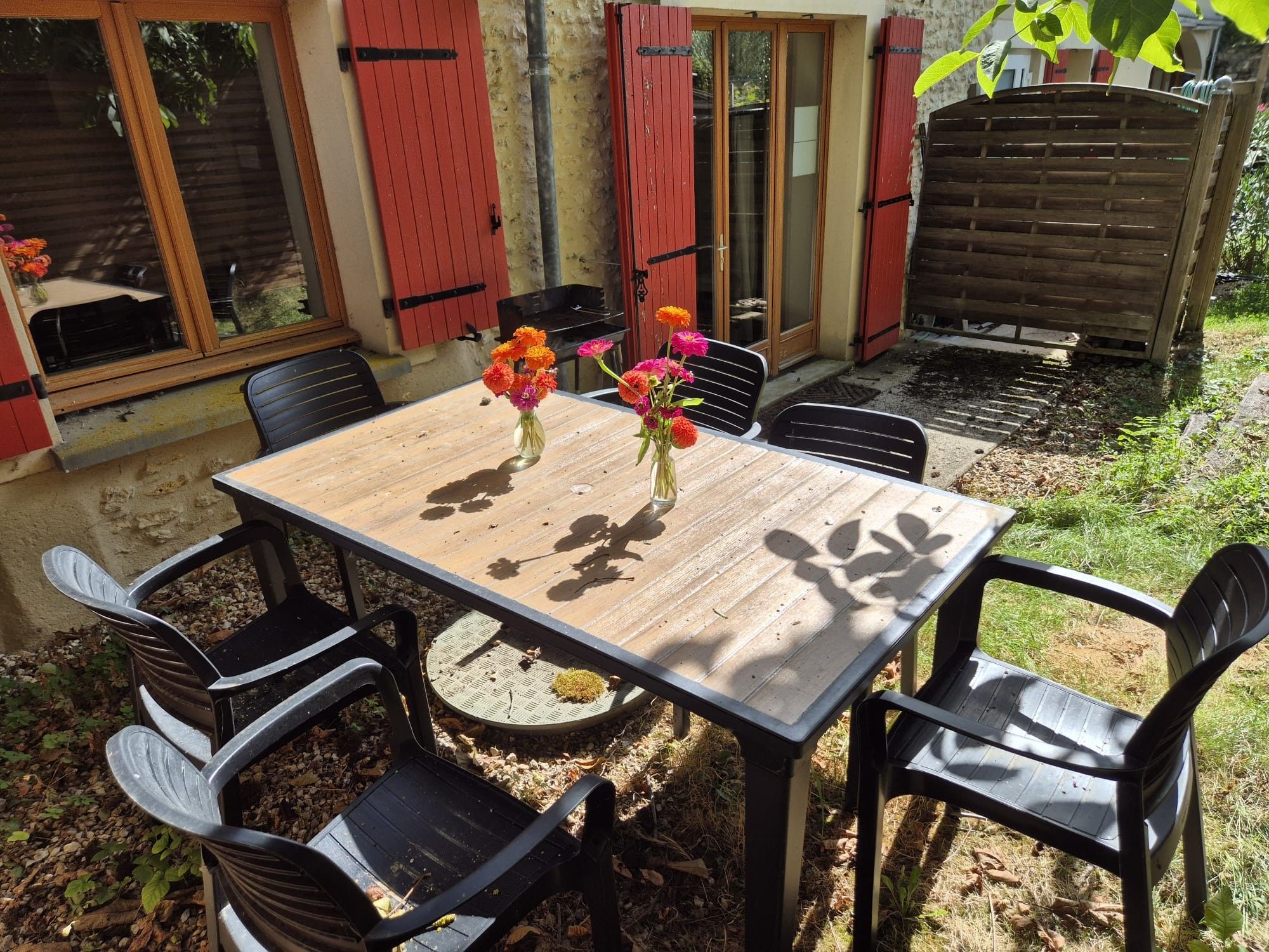 Een terras buiten met een houten tafel en zwarte stoelen.