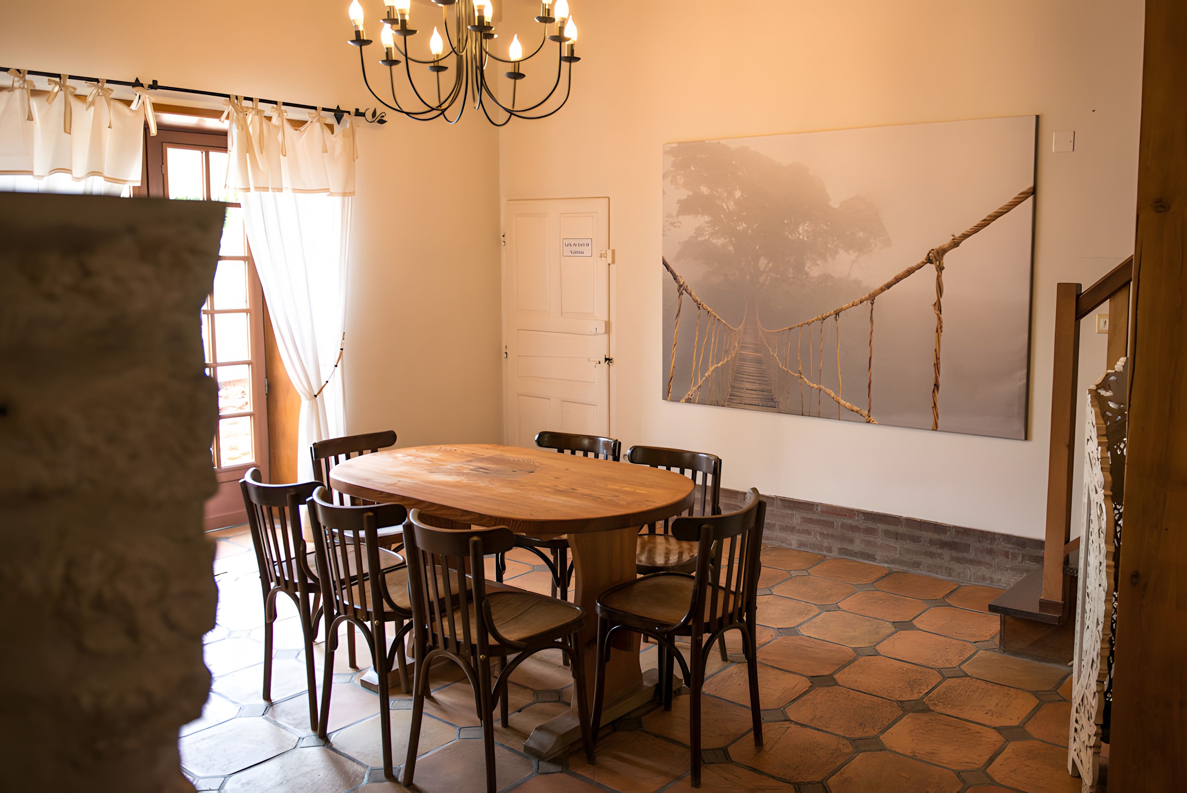 Un comedor con una mesa redonda de madera rodeada de sillas, una araña y un cuadro abstracto grande en la pared.