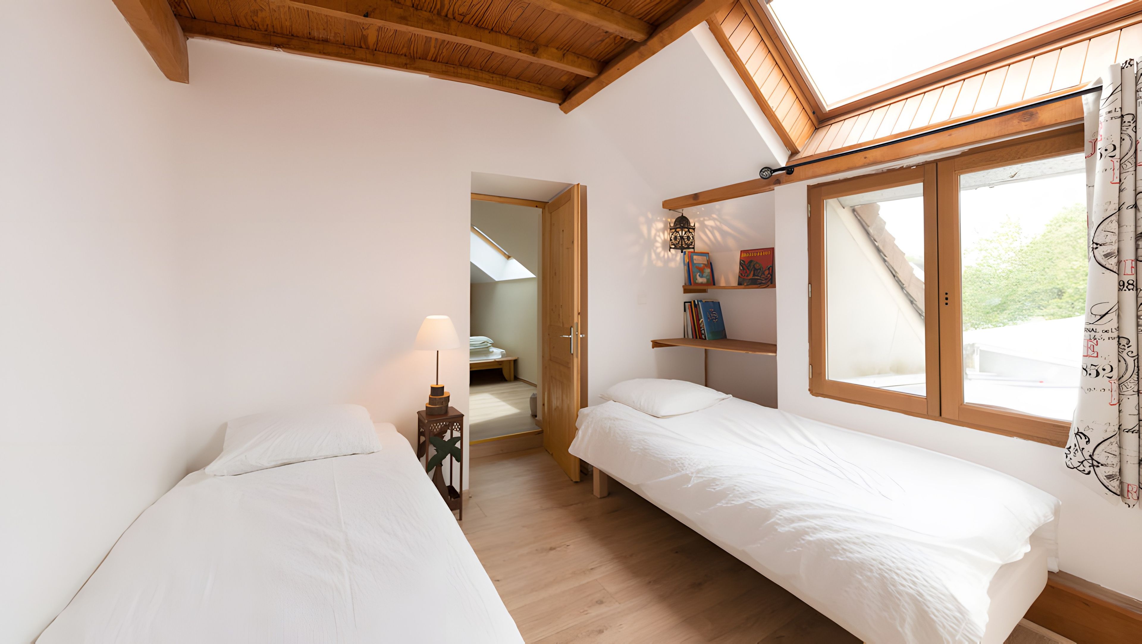 Une chambre avec deux lits, un puits de lumière, une fenêtre avec des rideaux et un plafond en bois.