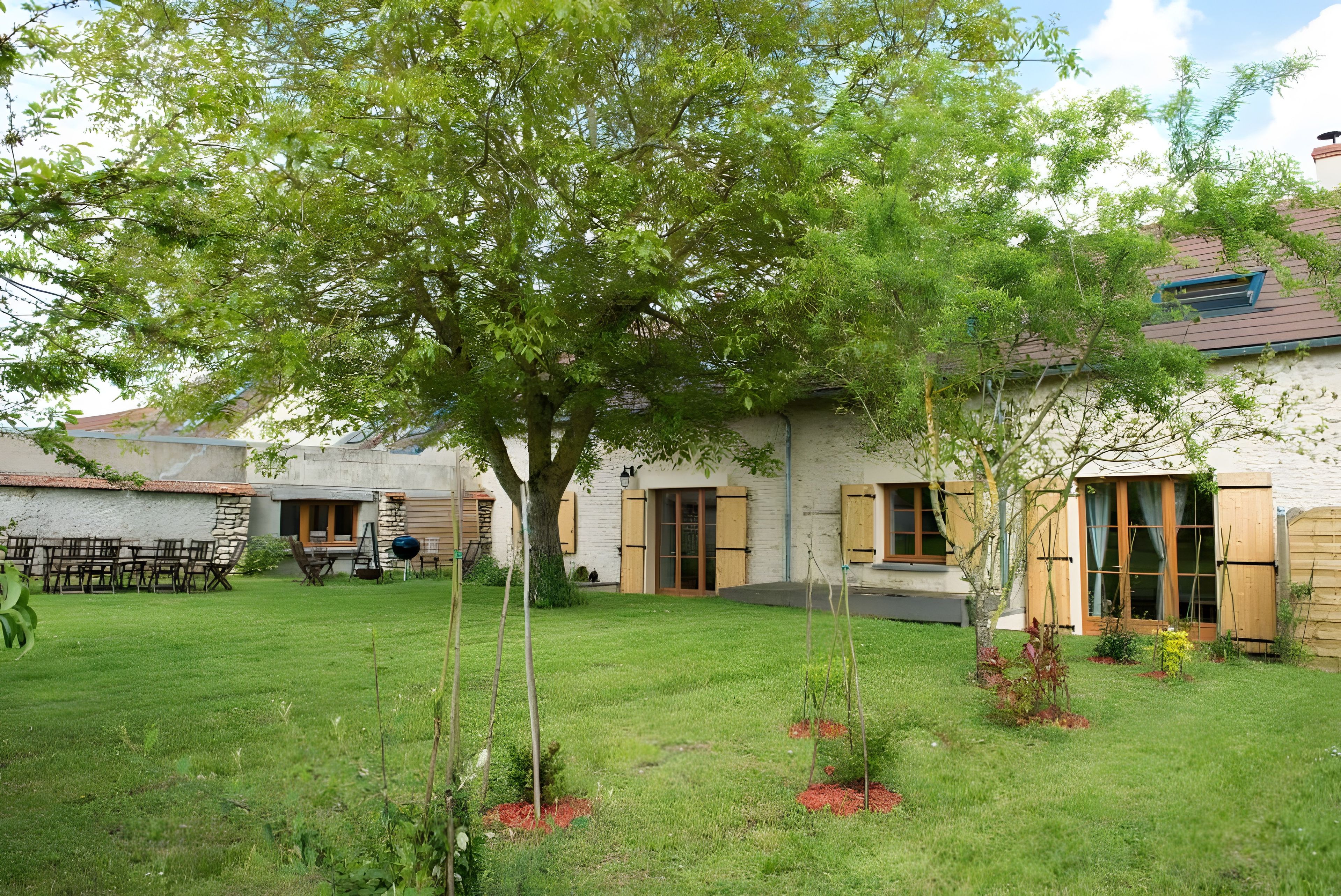 Ein Wohnhaus mit gepflegtem Rasen, einem großen Baum und einer Steinmauer.
