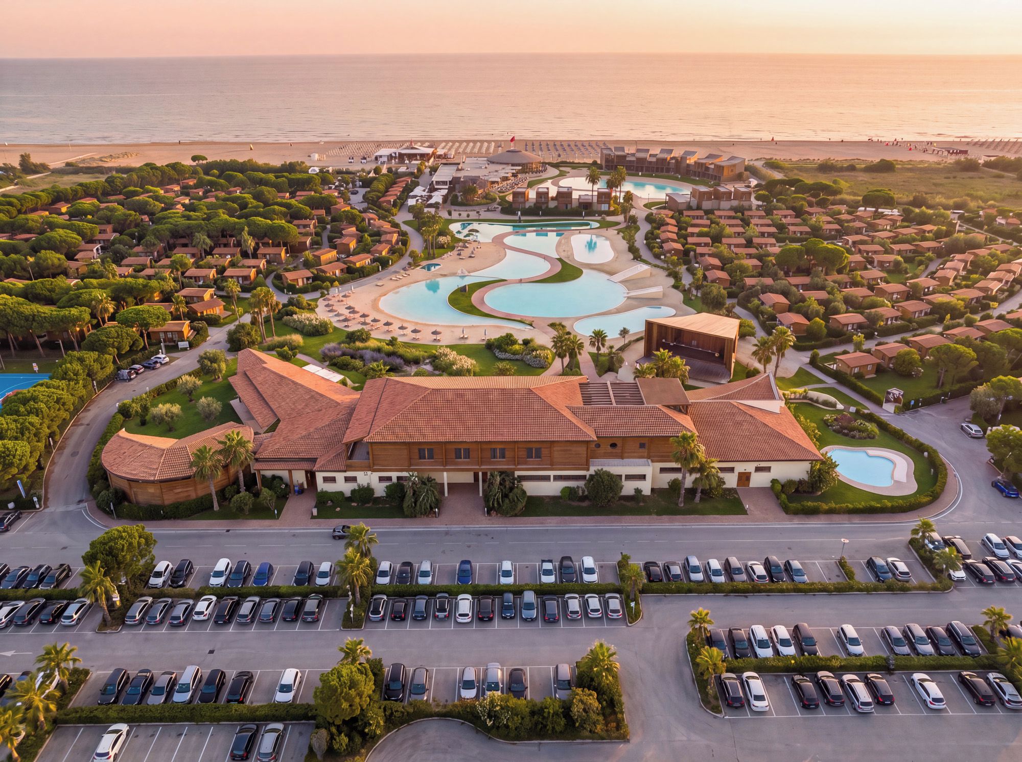 A resort with multiple swimming pools, a large parking lot, and a view of the ocean.
