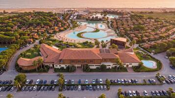 A resort with multiple swimming pools, a large parking lot, and a view of the ocean.