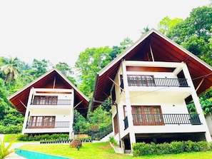 Two two-story buildings with balconies, surrounded by lush greenery.