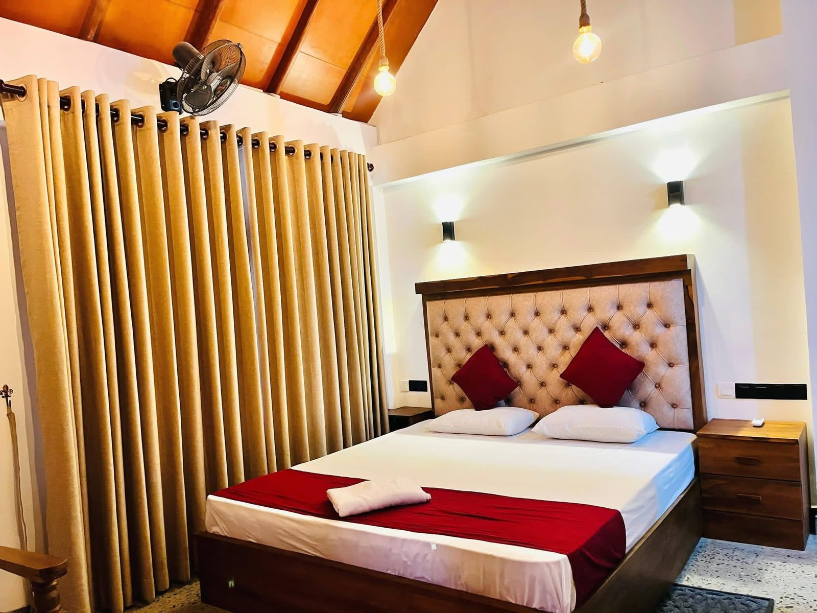 A hotel room with a bed, curtains, a fan, and a nightstand.