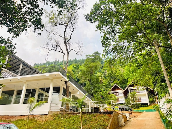 A modern building with a balcony, surrounded by lush greenery and trees.