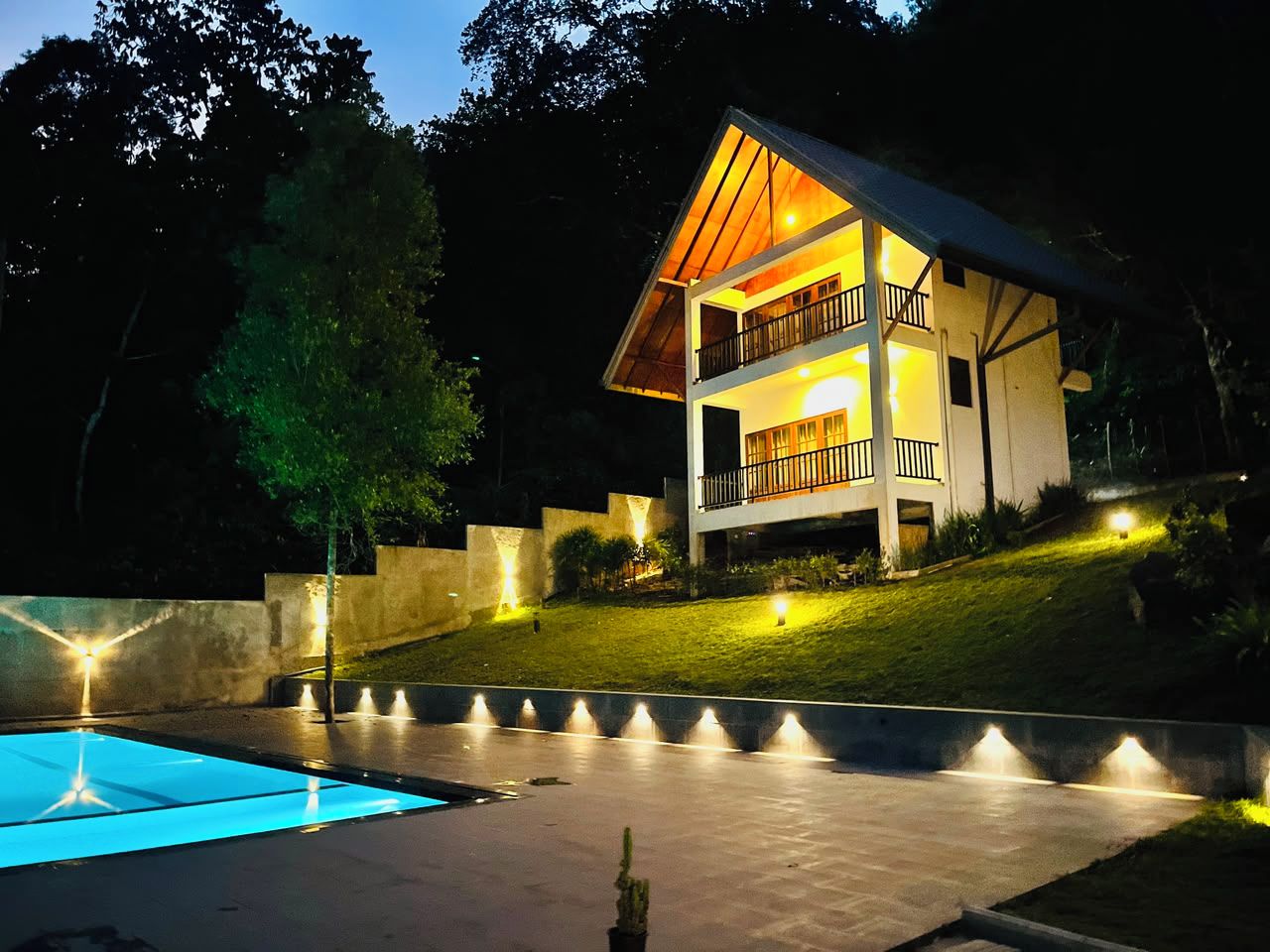 Une maison à deux étages avec un balcon, une piscine et un éclairage extérieur soigné.