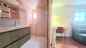 A compact kitchen with modern appliances, a dining area with a chair, and a window with patterned curtains. - New Listing (Royan)