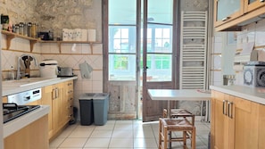 A kitchen with a stone wall, wooden cabinets, a built-in oven, and a window overlooking a garden. - New Listing (Royan)