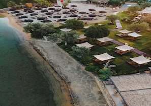 An aerial view of a resort with a beach, lounge areas with umbrellas, and a stone pathway leading to the water. - The Casa Cala Hotel (Bodrum)