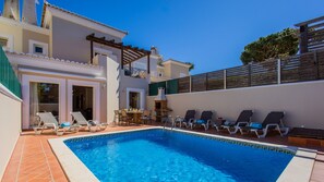 A swimming pool with lounge chairs and a table, surrounded by a building with a balcony and a fence. - Pine Haven. Vale do Lobo 3 Bedroom Townhouse (Vale do Lobo)