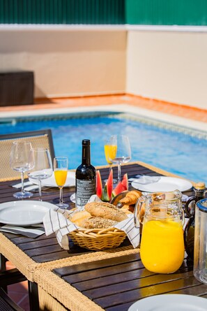 A dining table with a bottle, glasses, bread, and a jug of juice. - Pine Haven. Vale do Lobo 3 Bedroom Townhouse (Vale do Lobo)