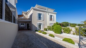 A modern two-story building with a paved driveway, a covered outdoor seating area, and a well-maintained garden with various plants and shrubs. - Pine Haven. Vale do Lobo 3 Bedroom Townhouse (Vale do Lobo)