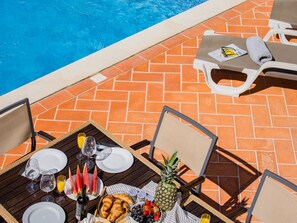A poolside dining area with a table set for two, chairs, and a pool in the background. - Pine Haven. Vale do Lobo 3 Bedroom Townhouse (Vale do Lobo)