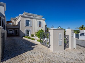 A residential building with a cobblestone driveway, a gated entrance, and a clear blue sky. - Pine Haven. Vale do Lobo 3 Bedroom Townhouse (Vale do Lobo)