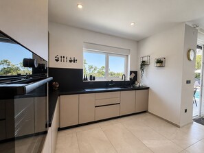 A modern kitchen with a black countertop, beige cabinets, a window with a view, and a sink. - Villa La Vie with heated pool (Garica)
