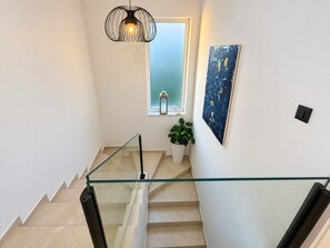 A modern staircase with glass railings, a decorative light fixture, a potted plant, and a piece of abstract art on the wall. - Villa La Vie with heated pool (Garica)