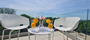 Un balcon avec deux chaises blanches, une table ronde et deux verres de jus d’orange garnis de tranches d’orange.