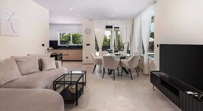 A modern living room with a sofa, coffee table, TV, and dining area with chairs and a table. - Villa La Vie with heated pool (Garica)