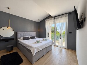 A modern bedroom with a grey upholstered bed, a round mirror, a black ottoman, and a black rug. - Villa La Vie with heated pool (Garica)