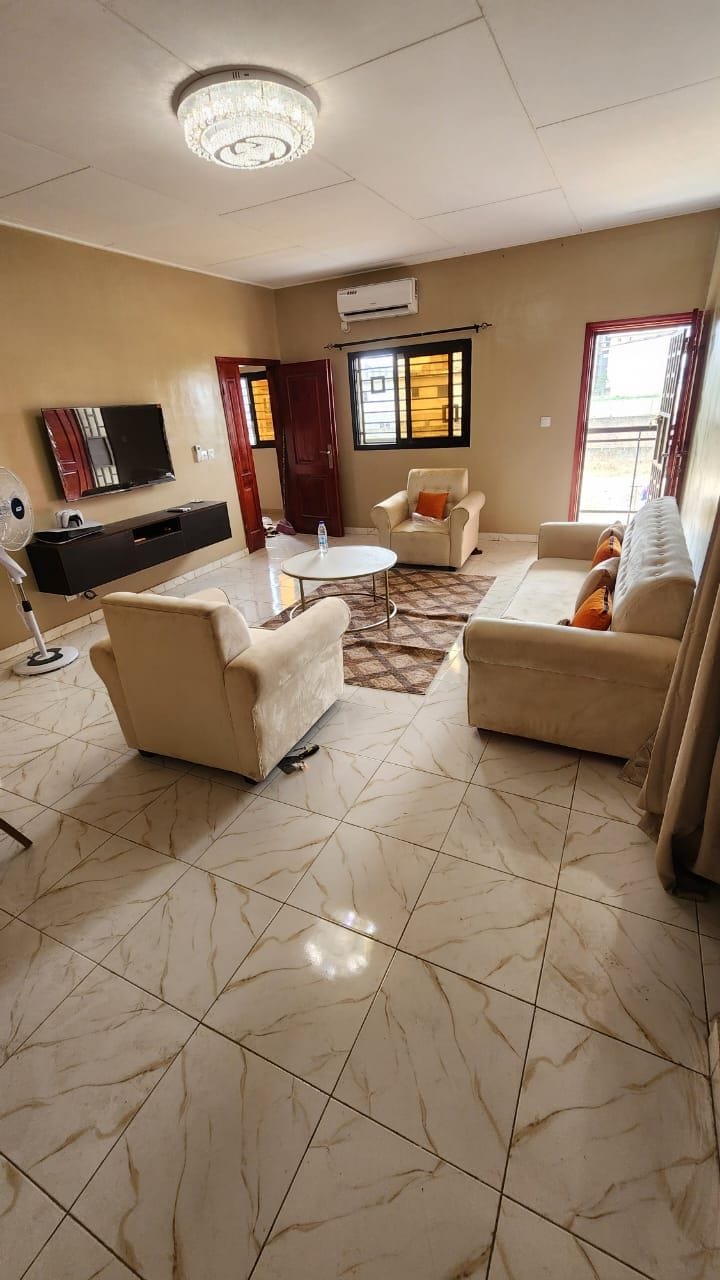 A living room with a flat-screen TV, two sofas, a coffee table, and a fan.