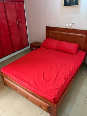A bed with a wooden frame and red bedding, a nightstand, and a red wardrobe. - New Listing (Abidjan)