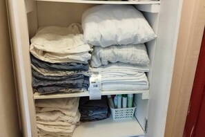 A closet with neatly folded bedding and storage bins.