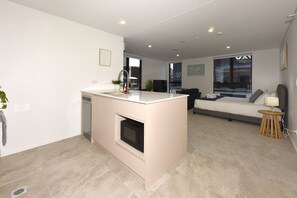 A modern kitchen with a built-in oven, a dining area with a sofa and a TV, and a bedroom with a bed and a bedside table. - Christchurch Studio With Queen Bed & Balcony (Christchurch)