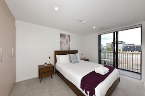 Ein modernes Schlafzimmer mit einem großen Bett, zwei Nachttischen, einem Fenster mit Blick auf die Stadt und einer Decke mit Einbaustrahlern.