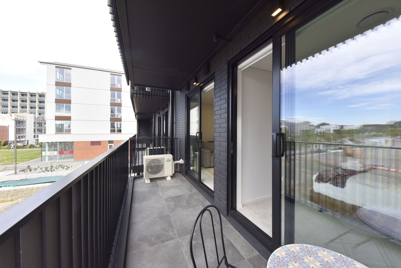 Ein Balkon mit Blick auf ein Schwimmbad und Gebäude, ein Tisch mit einem Stuhl und eine Klimaanlage.