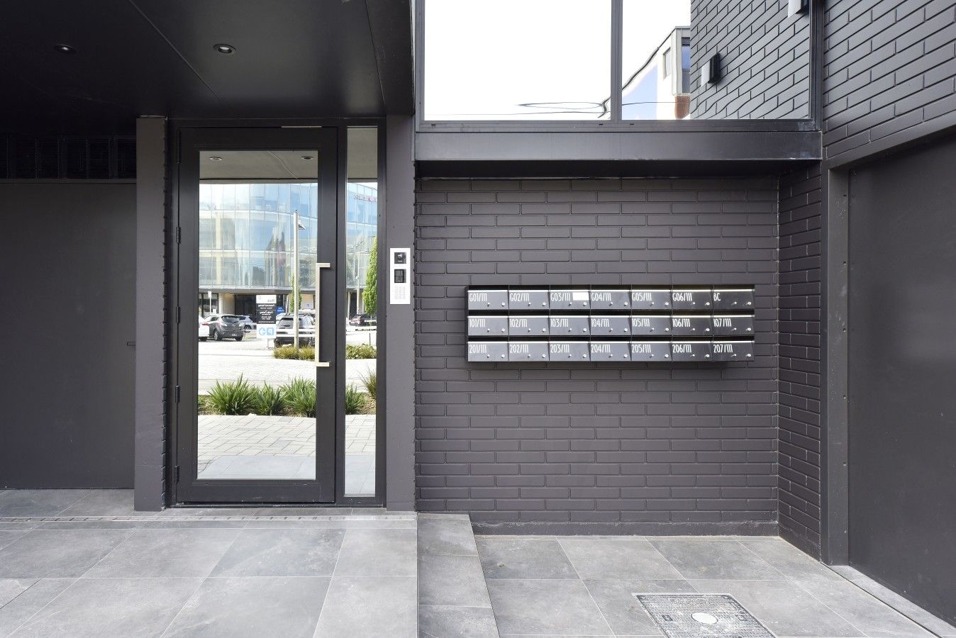 A modern building entrance with a glass door and a wall-mounted mailbox.