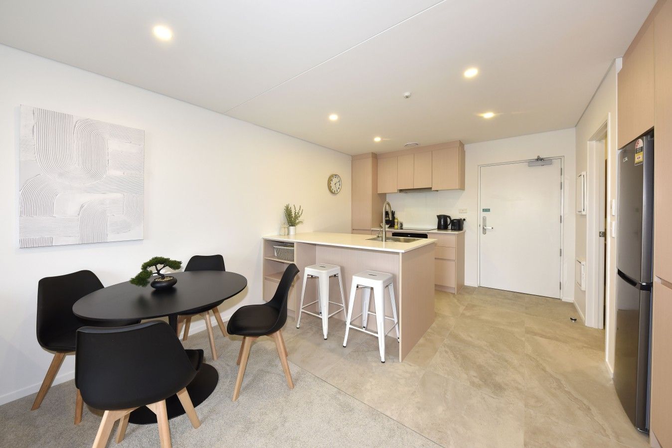A modern kitchen with a central island, a dining area with a round table and chairs, and a refrigerator.