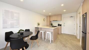 A modern kitchen with a central island, a dining area with a round table and chairs, and a refrigerator.